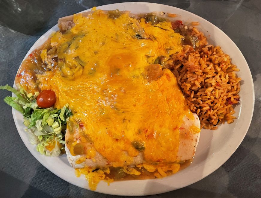 Plate of vegetarian Mexican food covered with chile sauce and melted cheese