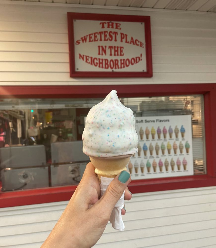 Cone with a white and confetti shell with a sign reading "The Sweetest Place in the Neighborhood"