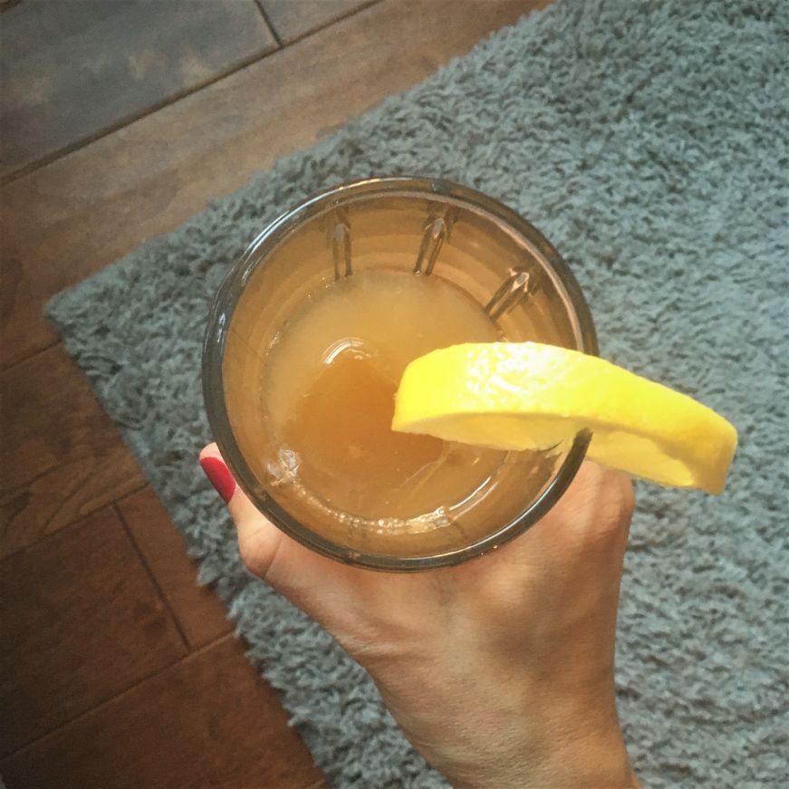 Top down view of a hand holding a cocktail garnished with a lemon slice