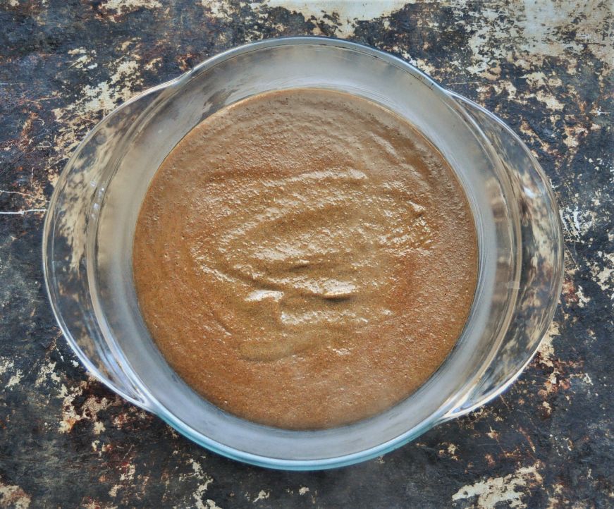 Glass casserole dish of cornmeal molasses pudding before baking