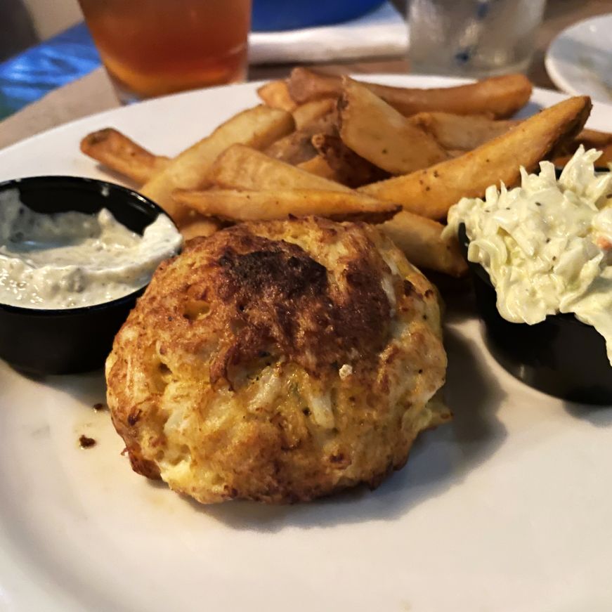Plate with a crab cake, french fries, and small cups of tartar sauce and coleslaw