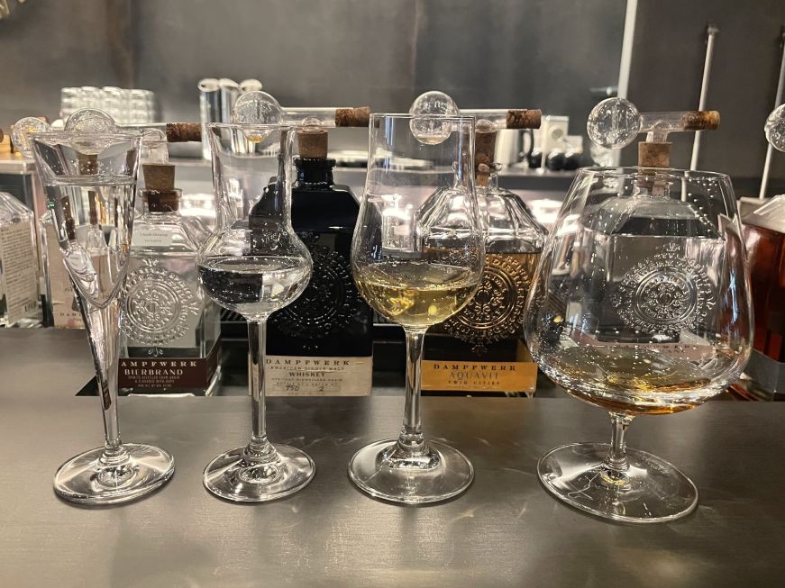Four stemmed glasses of brandy on a bar with bottles in background