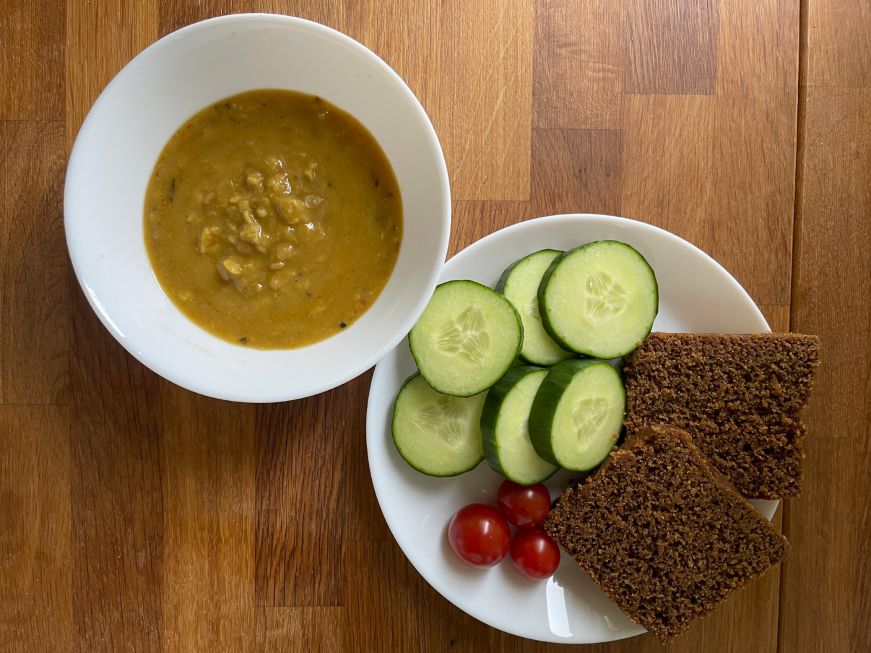 Bowl of soup and plate with sliced bread, cherry tomatoes, and sliced cucumbers