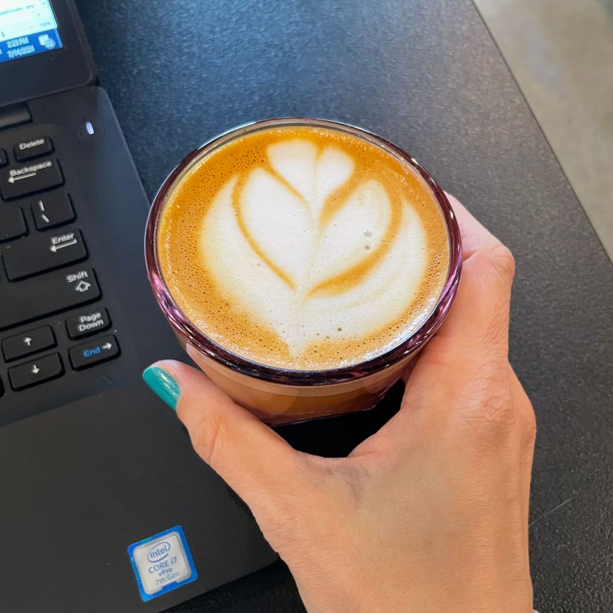 Hand holding cappuccino with foam art in a small pink glass