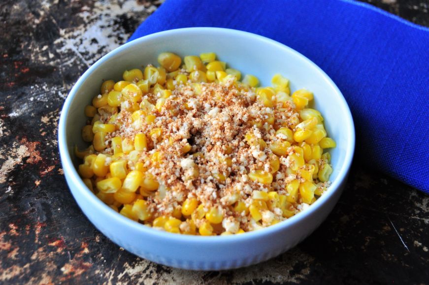 Bowl of corn garnished with cheese and chipotle powder