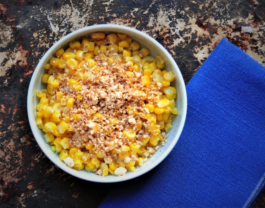 Bowl of corn garnished with cheese and chipotle powder