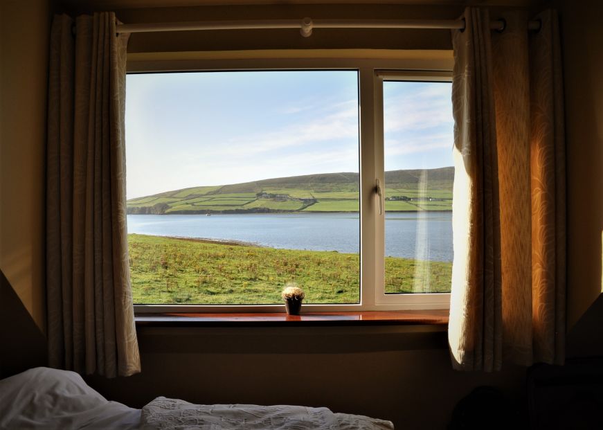 View of bay and rolling green hills through a bedroom window, Emlagh Lodge, Dingle, Ireland