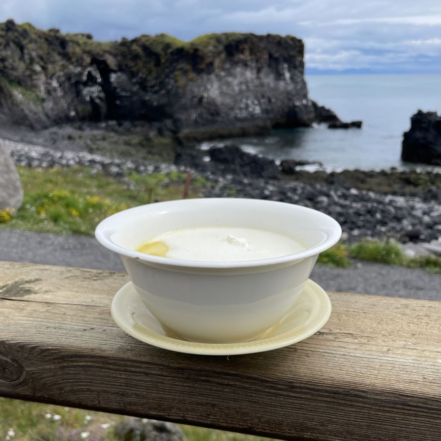 Fish soup, Fjöruhúsið Café Bowl of fish soup with a rocky cliff and cove in the background