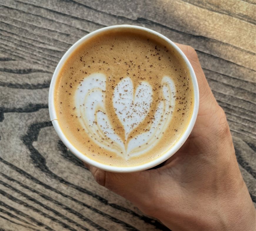 Hand holding a latte in a paper cup with latte art