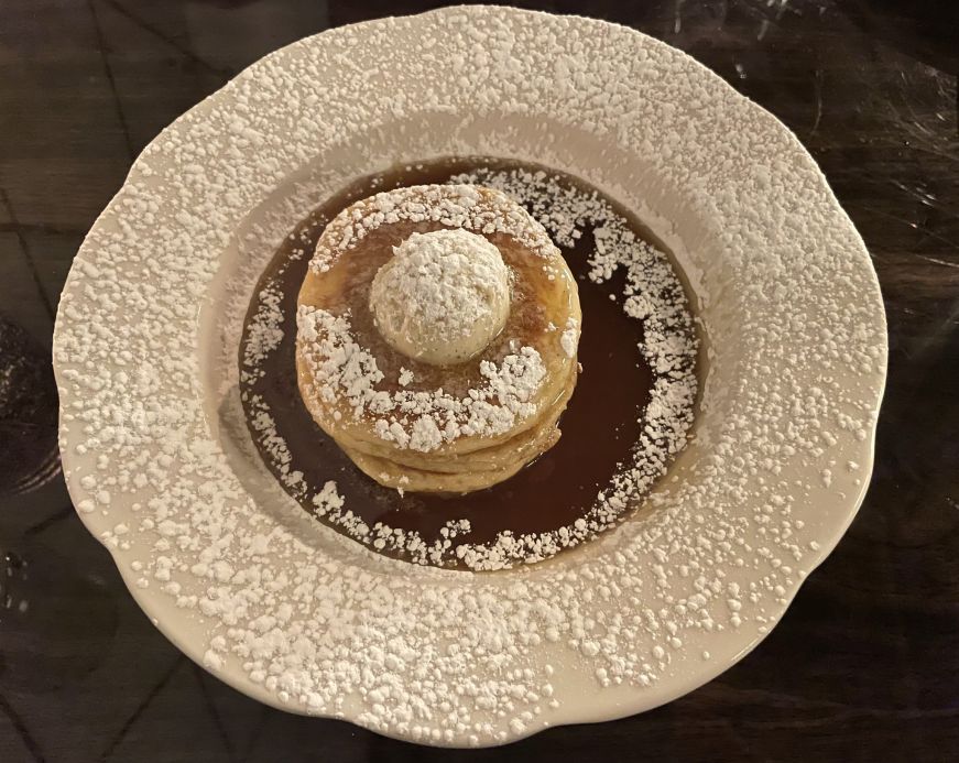 Pile of small pancakes surrounded by maple syrup