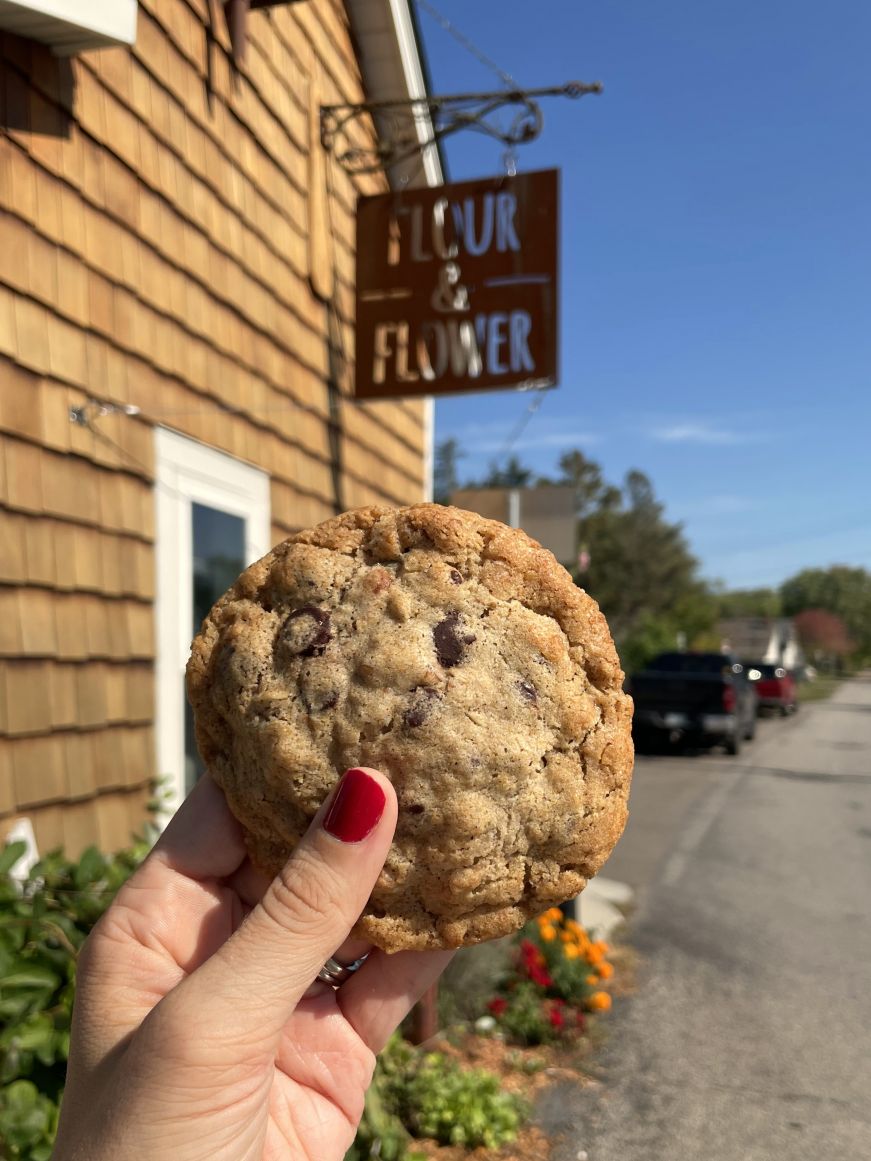 Stacy's hand holding a cookie with the Flour & Flower Bakery sign in the background
