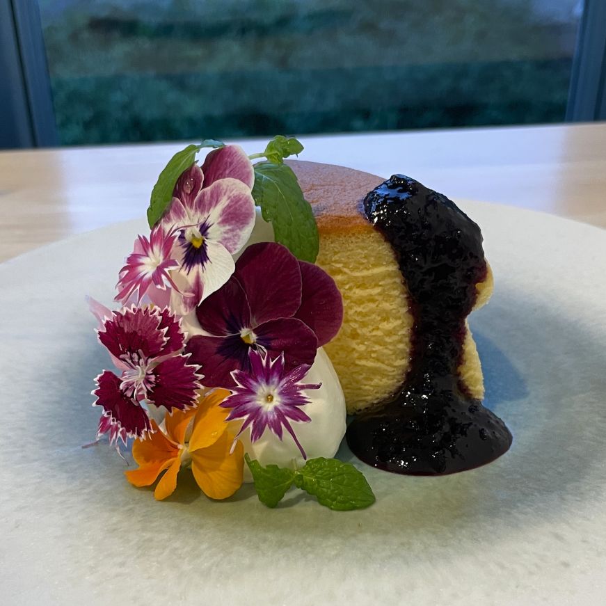 Piece of cheesecake garnished with flowers and blueberry sauce