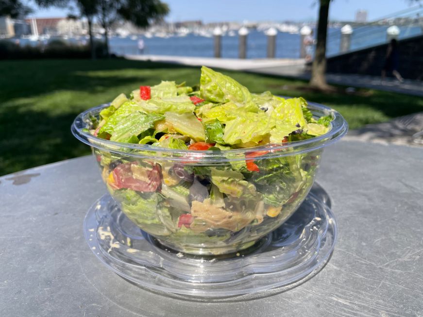Taco salad from Frank Anthony Seaport Market Salad in a plastic bowl sitting on a table in a park