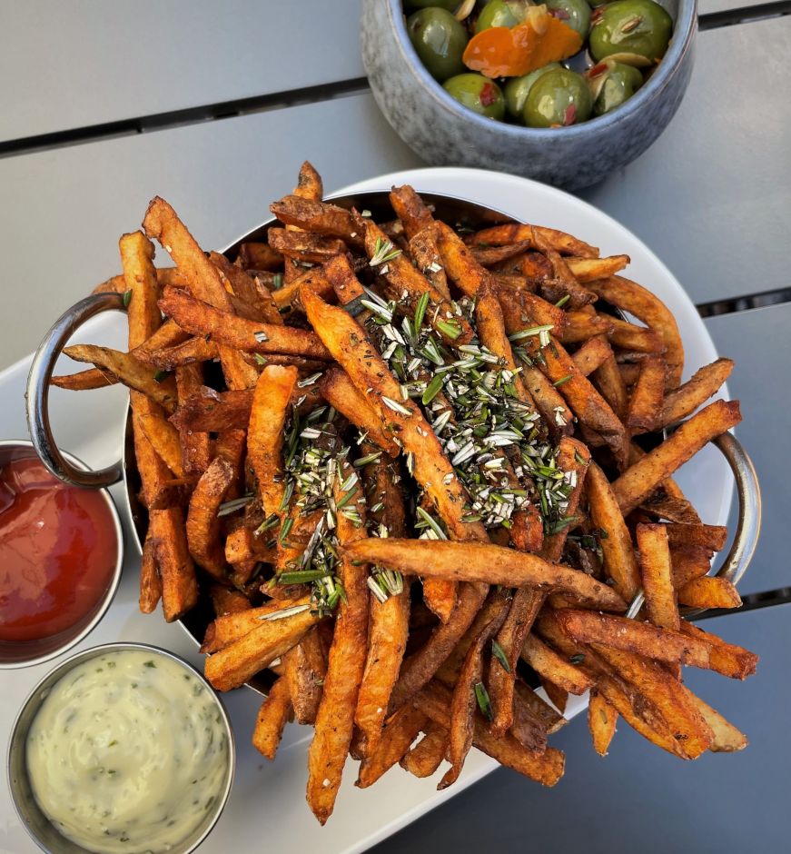 Bowl of fries topped with chopped rosemary and a small bowl of olives