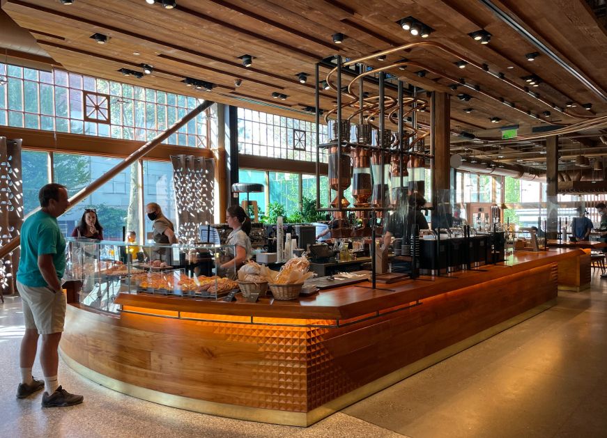 Wooden counter with coffee equipment, baristas, and a glass bakery case filled with pastries