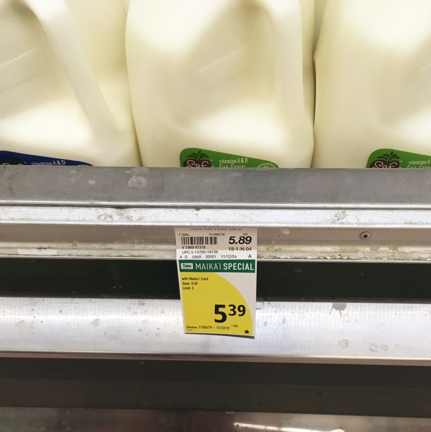 Three gallon-sized jugs of milk with a price sign reading "$5.39" at a Hawaiian grocery store