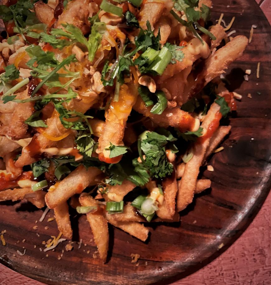 Wooden platter of fries drizzled with peanut and hoisin sauces and garnished with cilantro and chopped peanuts
