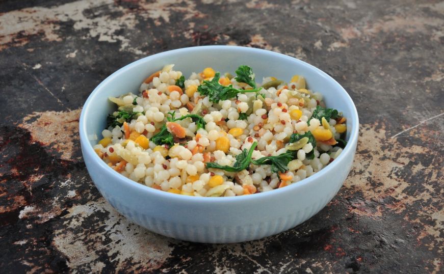 Bowl of couscous, orzo, lentil, and quinoa pilaf garnished with parsley