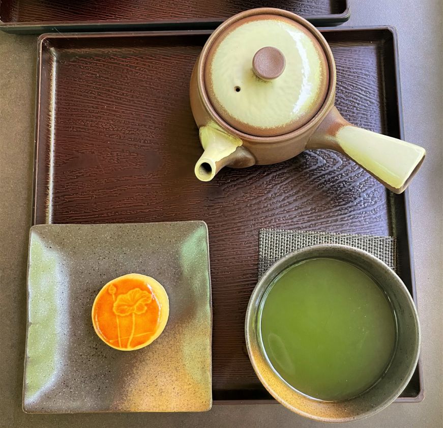 Top down view of a tea tray with a small teapot, cup of tea, and a small cake