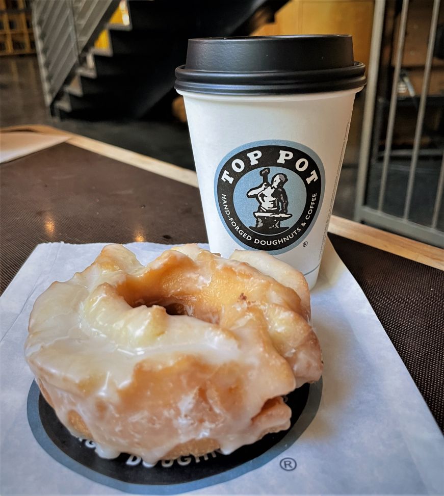 Glazed old fashioned doughnut and a paper cup of coffee with the logo for Top Pot Doughnuts