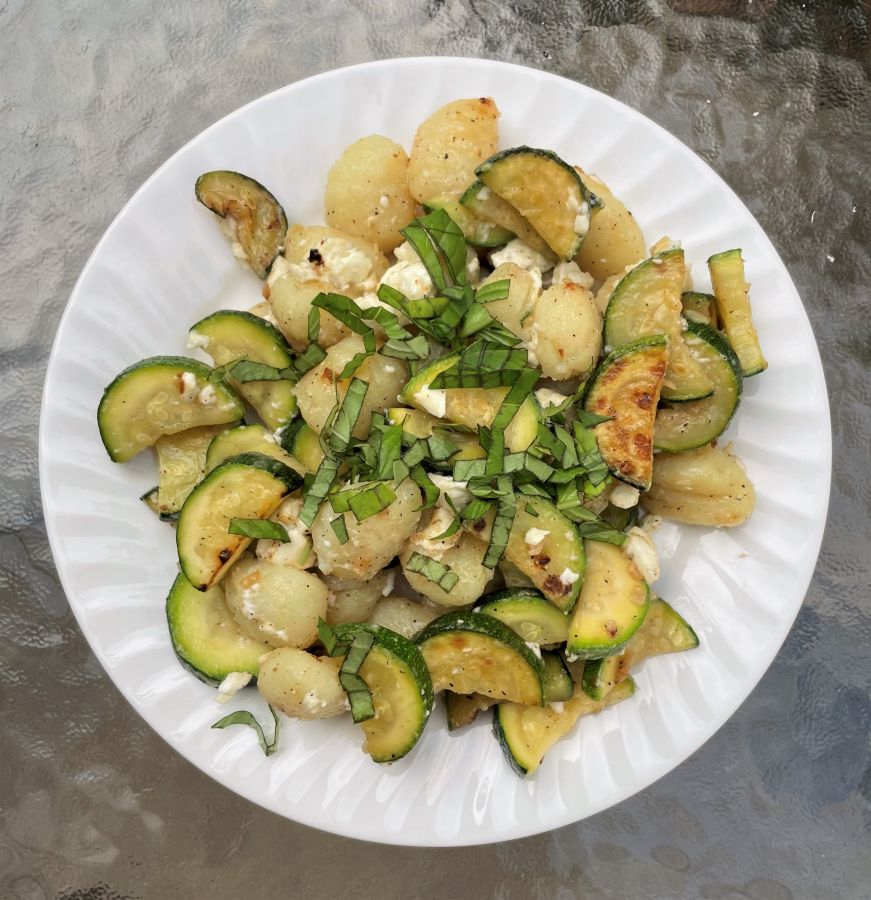 Plate of gnocchi mixed with sauteed zucchini and feta and topped with fresh basil
