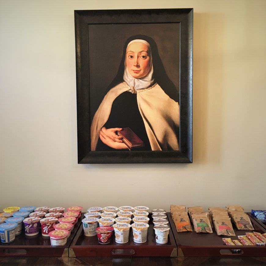 Painting of nun on wall behind a table stocked with packaged breakfast items