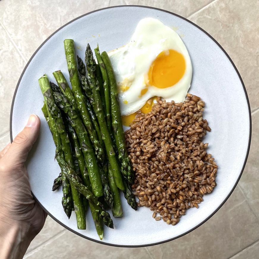 Grilled asparagus, egg, and farro on a 10.5" Coupe entree plate Grilled asparagus, egg, and farro on a white plate with a dark brown edge