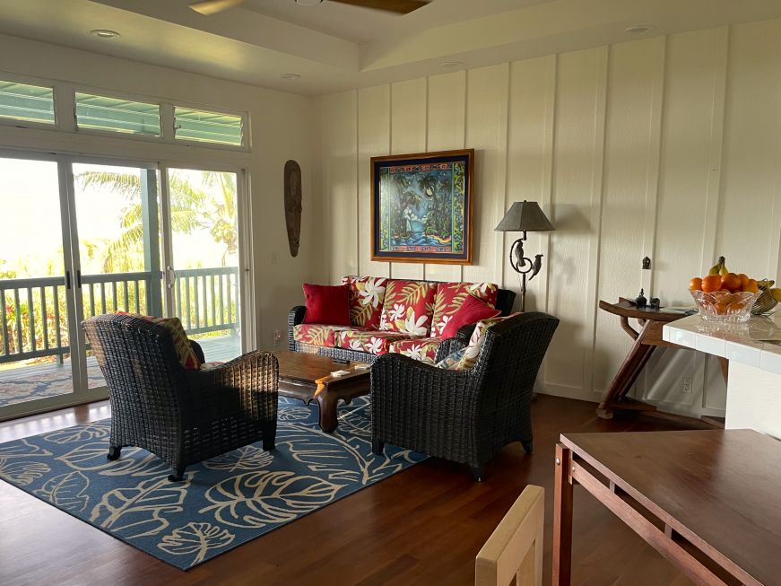 Large living room opening onto a porch with a view of the ocean and palm trees