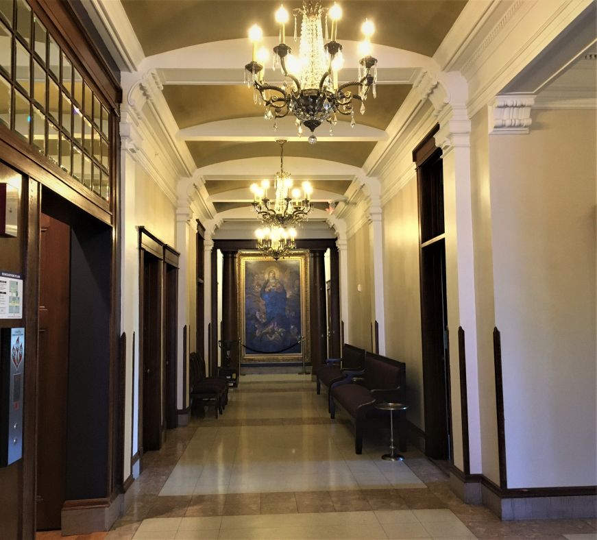 Hallway with ornate woodwork, religiously-themed oil paintings, and chandeliers