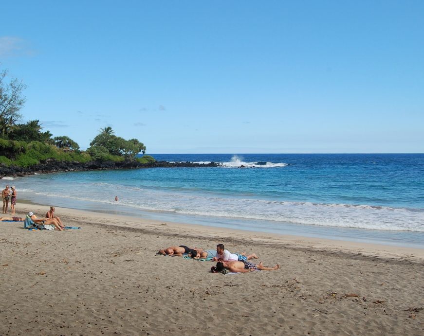 People sunbathing on white sandy beach with ocean in the background