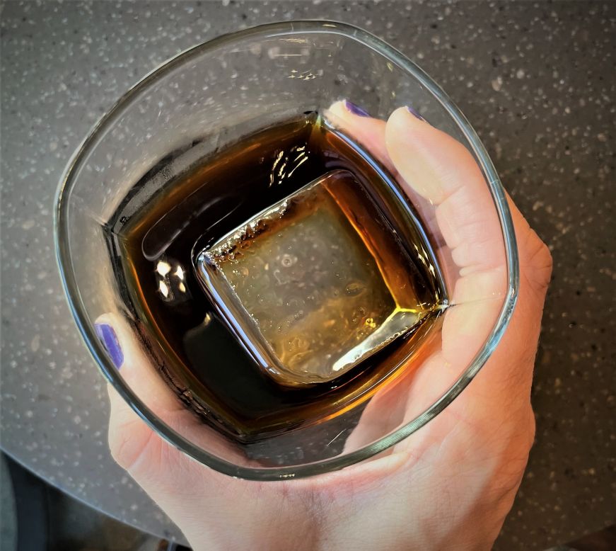 Top down view of a hand holding a rocks glass with a large ice cube and cold brew
