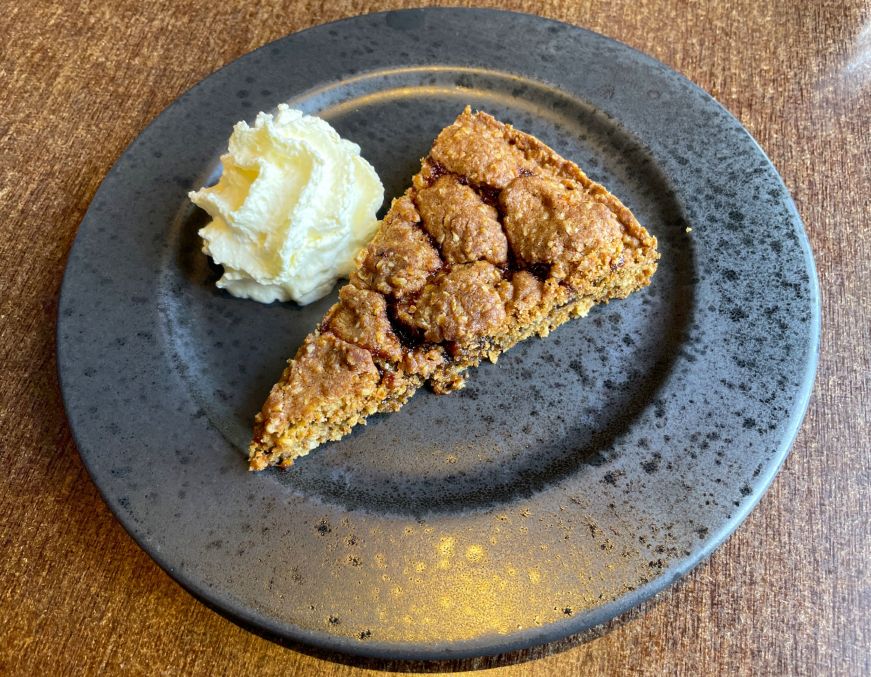 Hjónabandssæla, Vegamót Tart with an oat crust and rhubarb filling on a blue plate with a dollop of whipped cream on the side