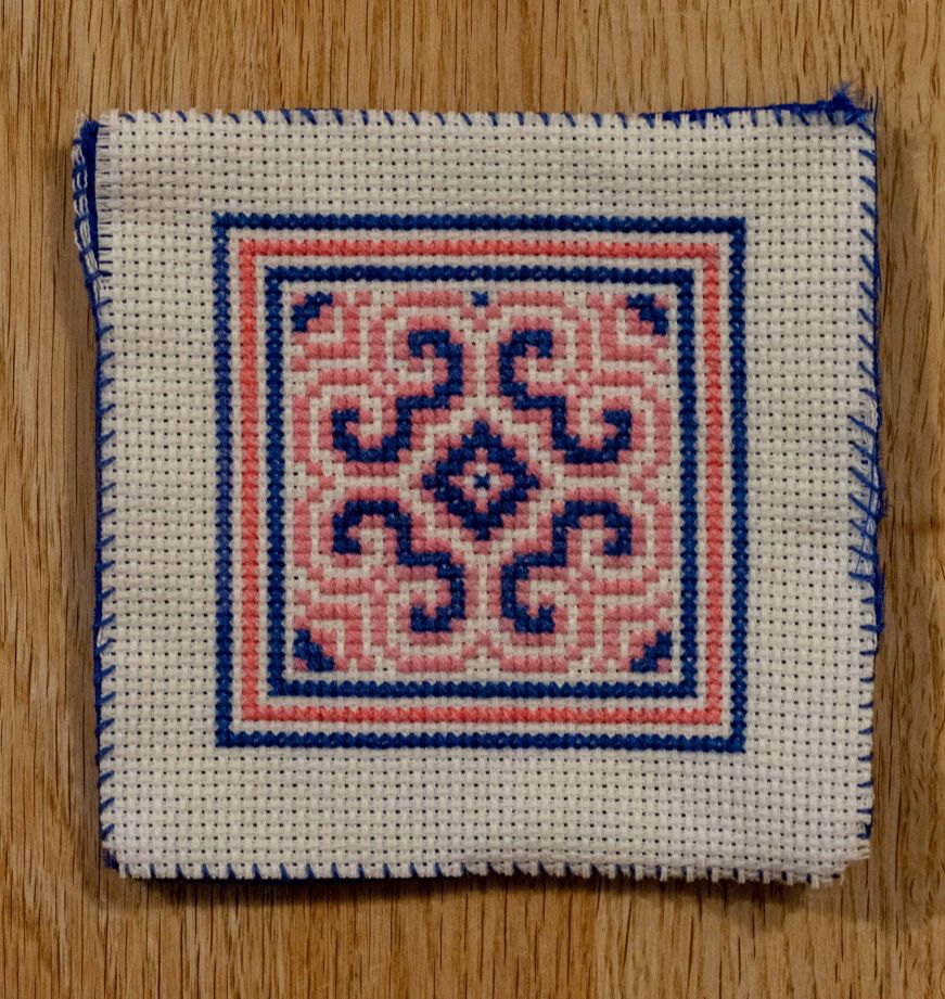 Embroidered coaster with a geometric design in blue and pink