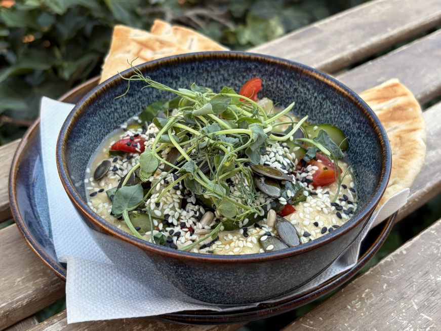 Bowl of hummus topped with cherry tomatoes, microgreens, and sesame and pumpkin seeds