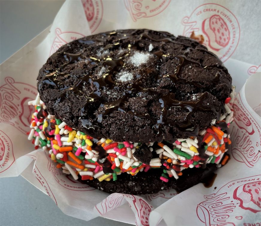 Two chocolate cookies sandwiching an ice cream filling rolled in sprinkles