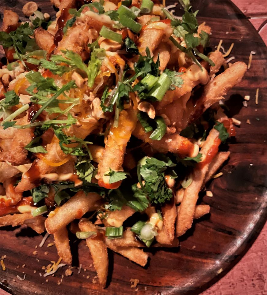 Fries topped with shredded cheese, green onions, chopped peanuts, and cilantro