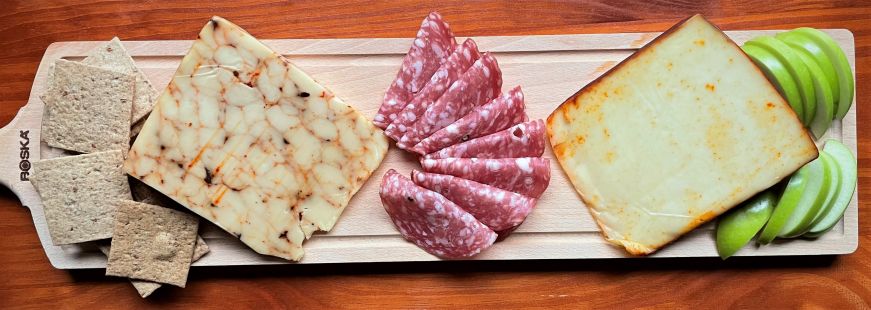 Rectangular cheese board with two blocks of cheese, crackers, salami, and sliced apples arranged with space in between each food item