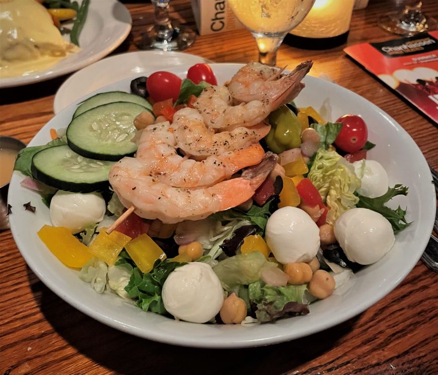 Lettuce salad topped with a skewer of grilled shrimp