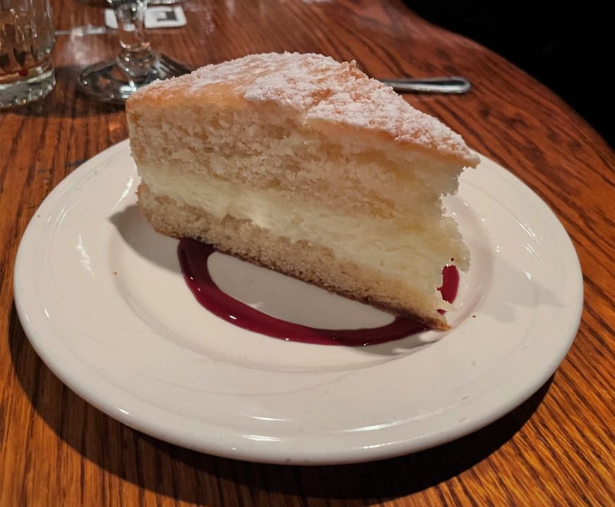 Slice of white cake with a white cream filling and berry sauce garnish on the plate