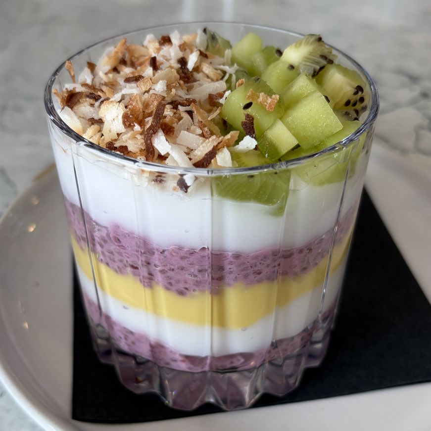 Layered parfait of yogurt, chia pudding, and mango curd topped with toasted coconut and kiwi