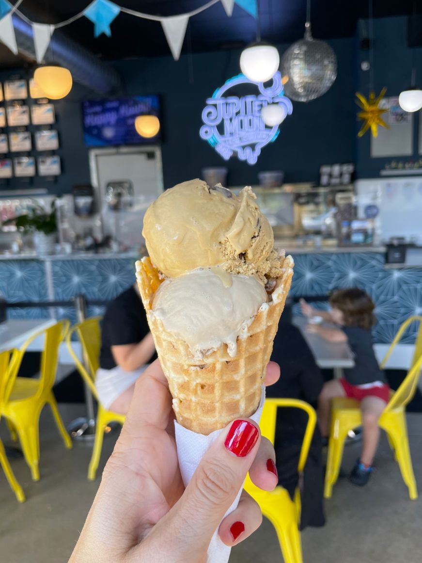 Stacy's hand holding an ice cream cone with the Jupiter Moon Ice Cream neon sign in the background