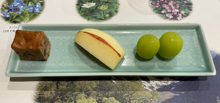Plate with a piece of cake, slice of apple, and two grapes