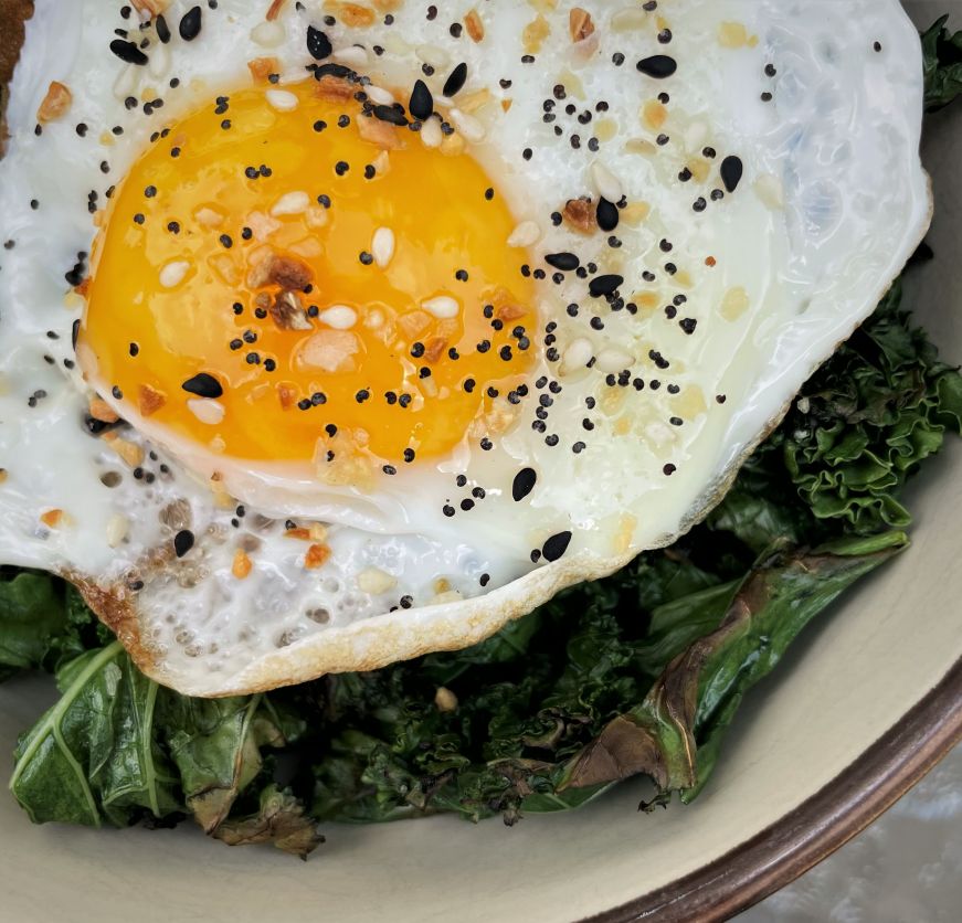 Close up of a fried egg on top of sauteed kale