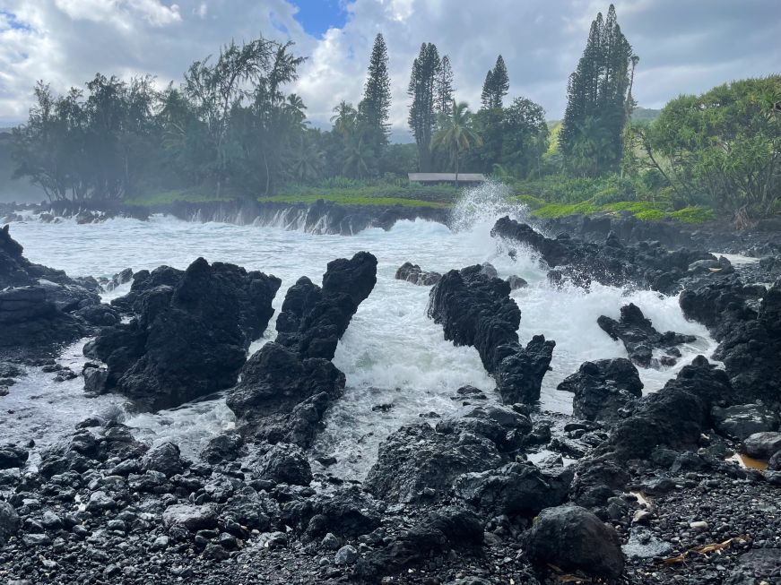 Large waves crashing into a bay surrounded by jagged black lava rocks