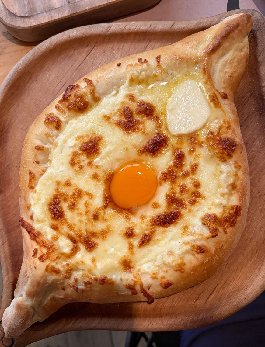 Oval shaped bread with melted cheese, an egg yolk, and pat of butter in the center