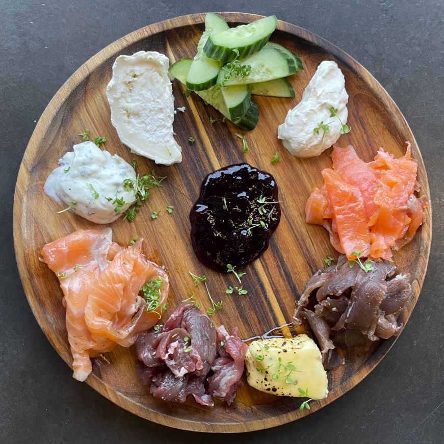 Krauma platter, Krauma Top down view of a wooden platter with cheeses, cured salmon and goat, skyr, jam, and sliced cucumber
