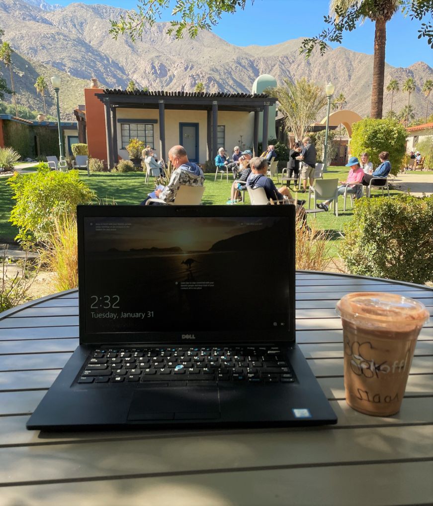 Laptop and iced coffee sitting on table with mountains in the background