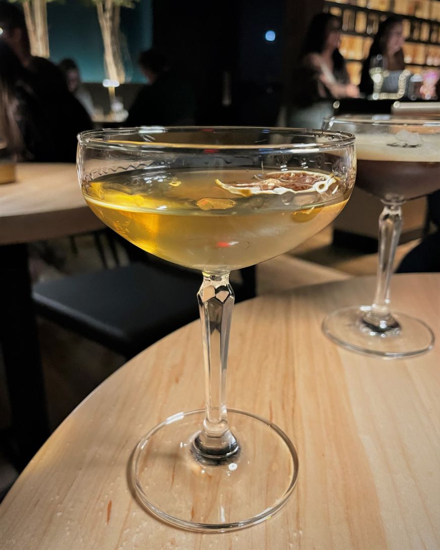Cocktail in a coupe glass garnished with a dried orange slice