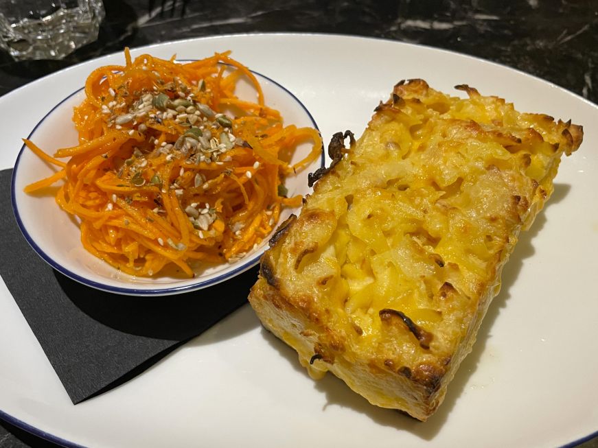Rectangular piece of mac and cheese kugel with carrot slaw on the side