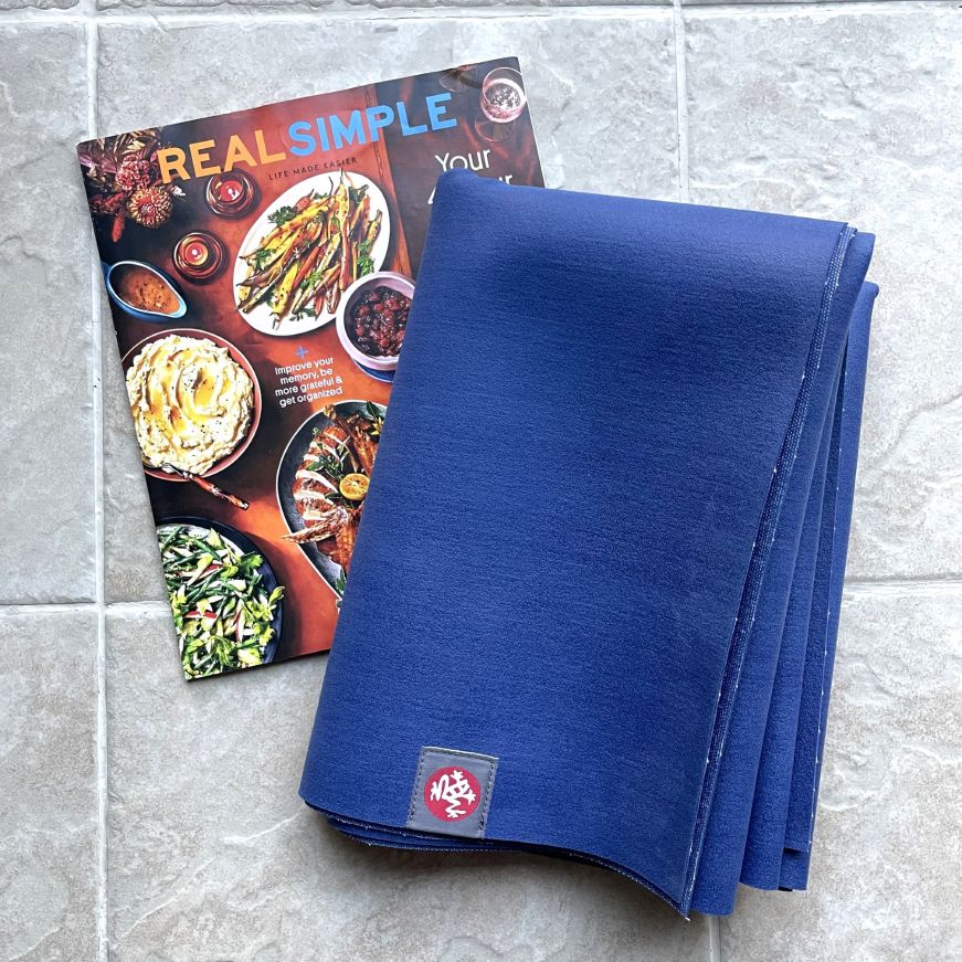 Maduka eKO Superlite Travel Yoga Mat Folded navy yoga mat with a magazine for scale